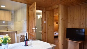 A wooden cabin interior with a dining table set for two, a television, and a visible bathroom. - Bungalows an der Ostsee (Kołobrzeg)