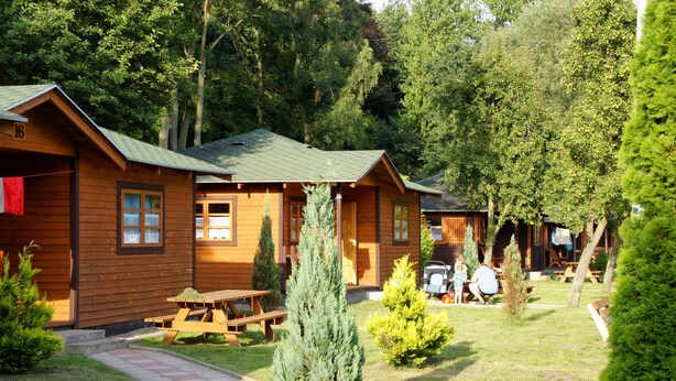 A row of wooden cabins with picnic tables in a forested area. - Bungalows an der Ostsee (Kołobrzeg)