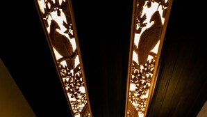 Un couloir aux murs lambrés et au plafond orné de motifs complexes découpés. On y trouve des tabourets de bar et un luminaire suspendu.