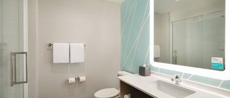 Une salle de bain moderne avec une douche à parois de verre, des toilettes blanches, un lavabo avec un miroir et un porte-serviettes.