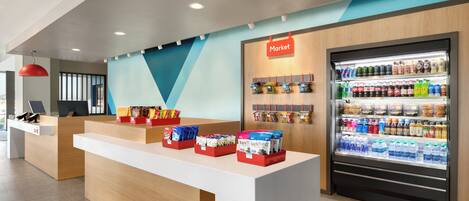 Un espace d’accueil moderne comprenant un comptoir, un réfrigérateur rempli de boissons et un panneau mural indiquant qu’il s’agit d’une épicerie.