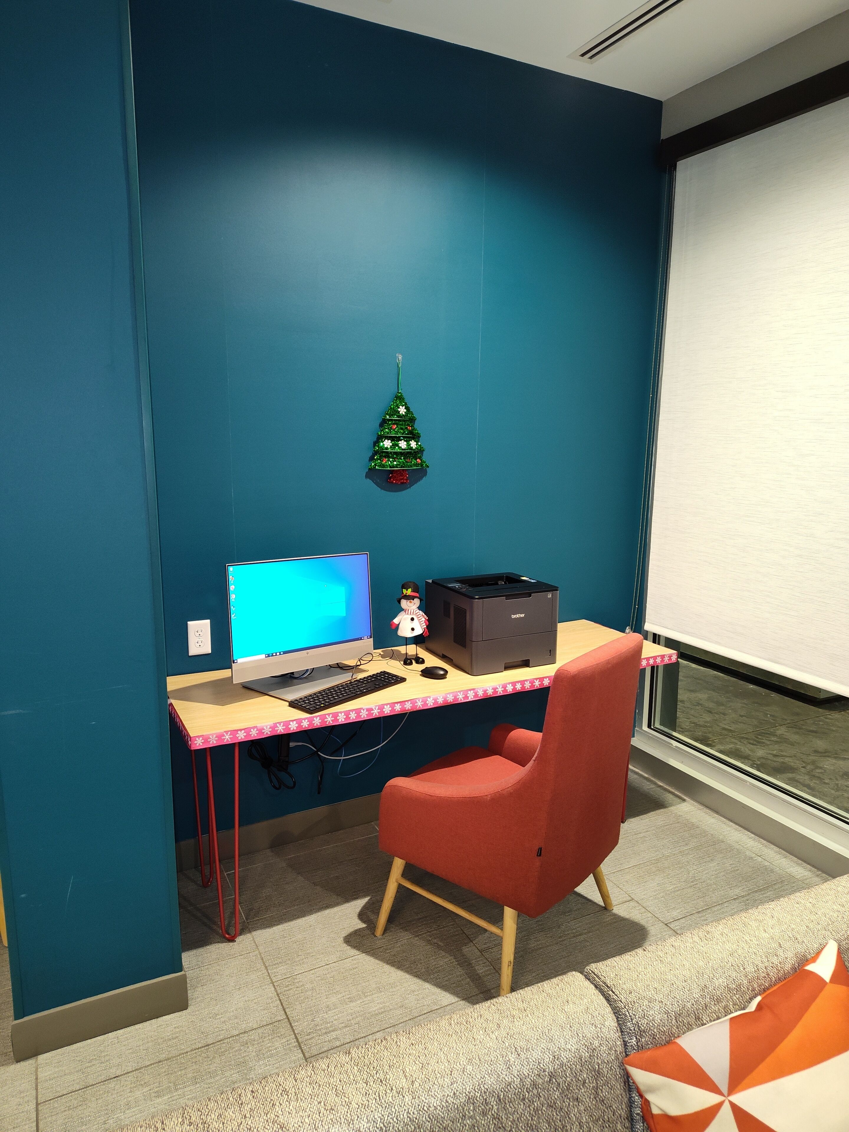 Een werkplek met een bureau, computer, printer en een rode stoel.