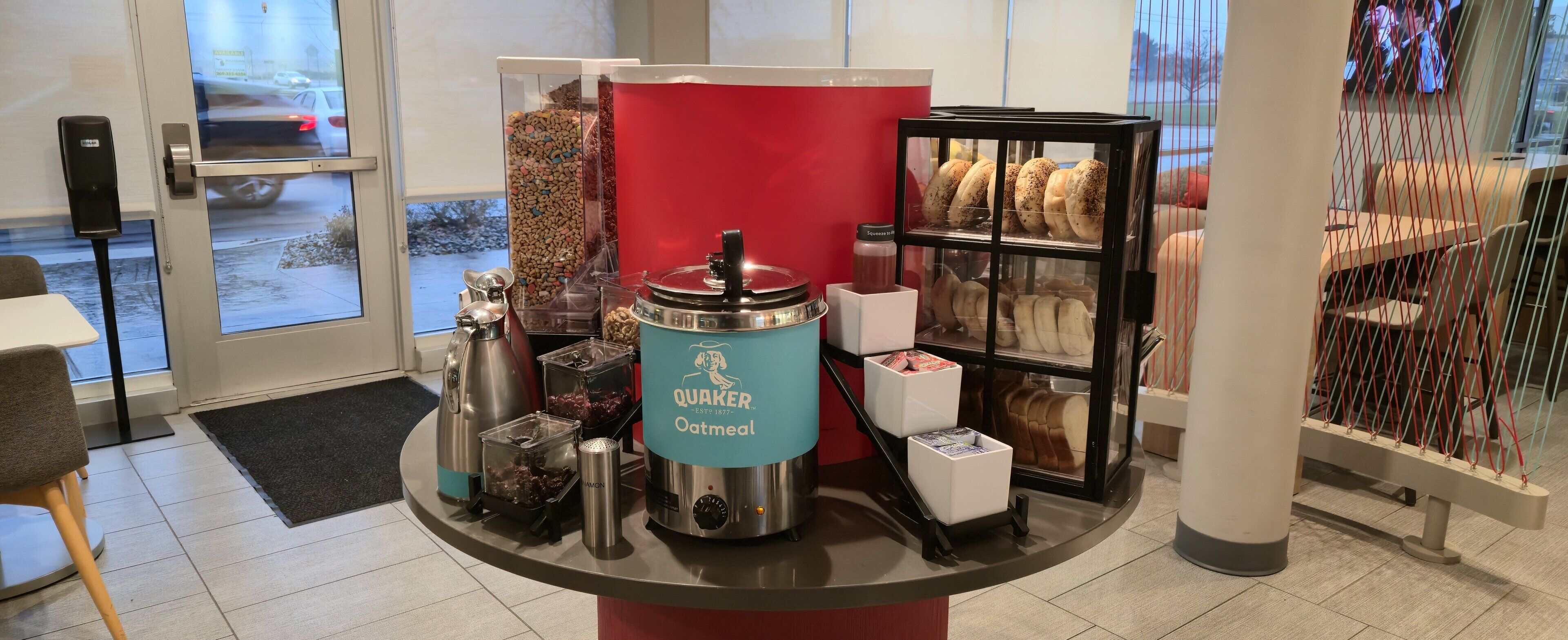 A kitchen counter with a Quaker Oatmeal coffee maker, a coffee grinder, and a display case with pastries.