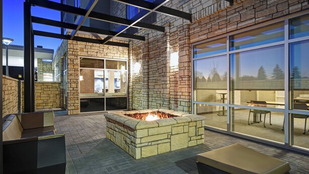 An outdoor patio with a stone fire pit, seating, and a glass wall offering views of the interior. - SpringHill Suites by Marriott St. Paul Arden Hills (Arden Hills)