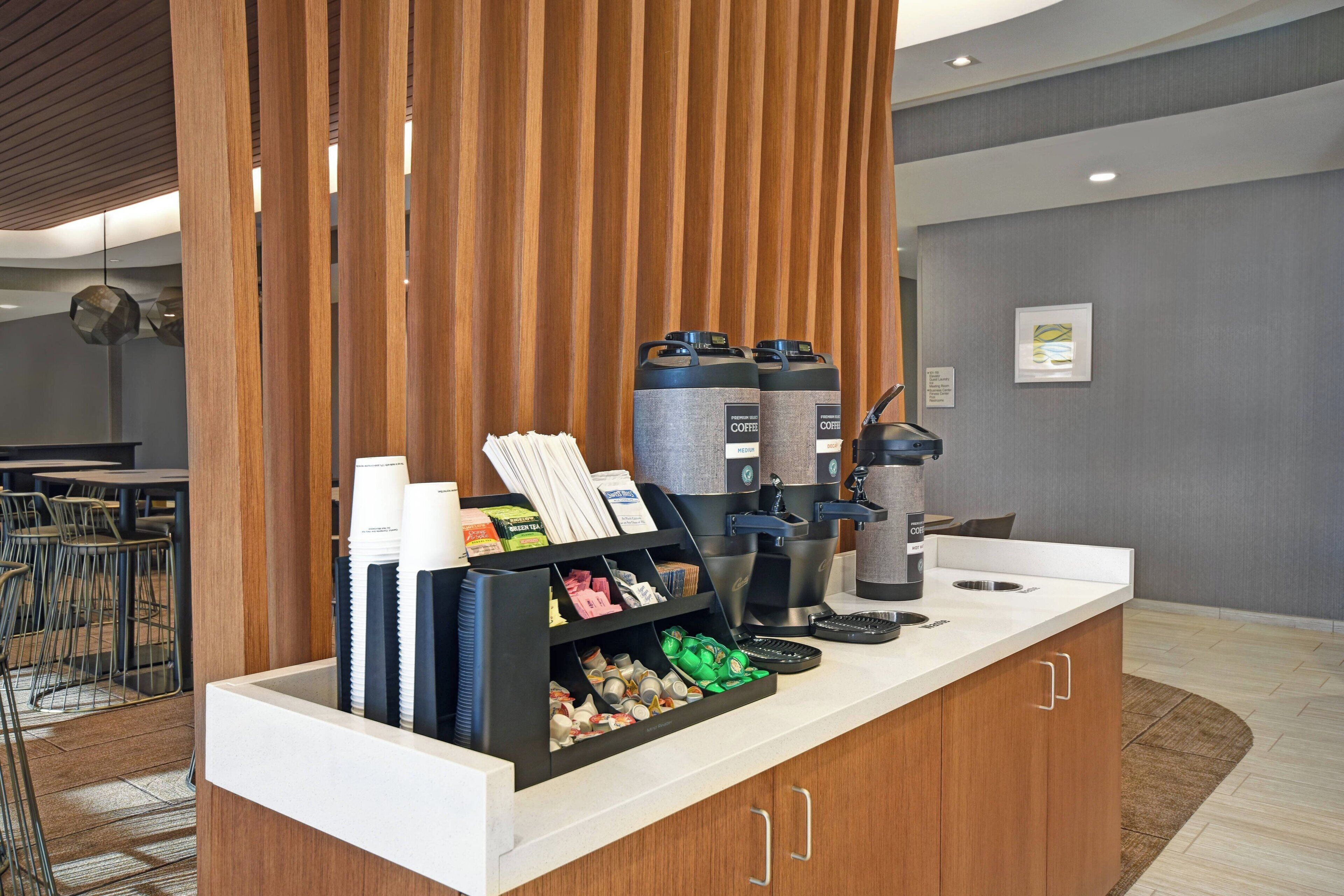 A hotel reception area with a coffee station, including coffee makers, cups, and a variety of coffee beans.