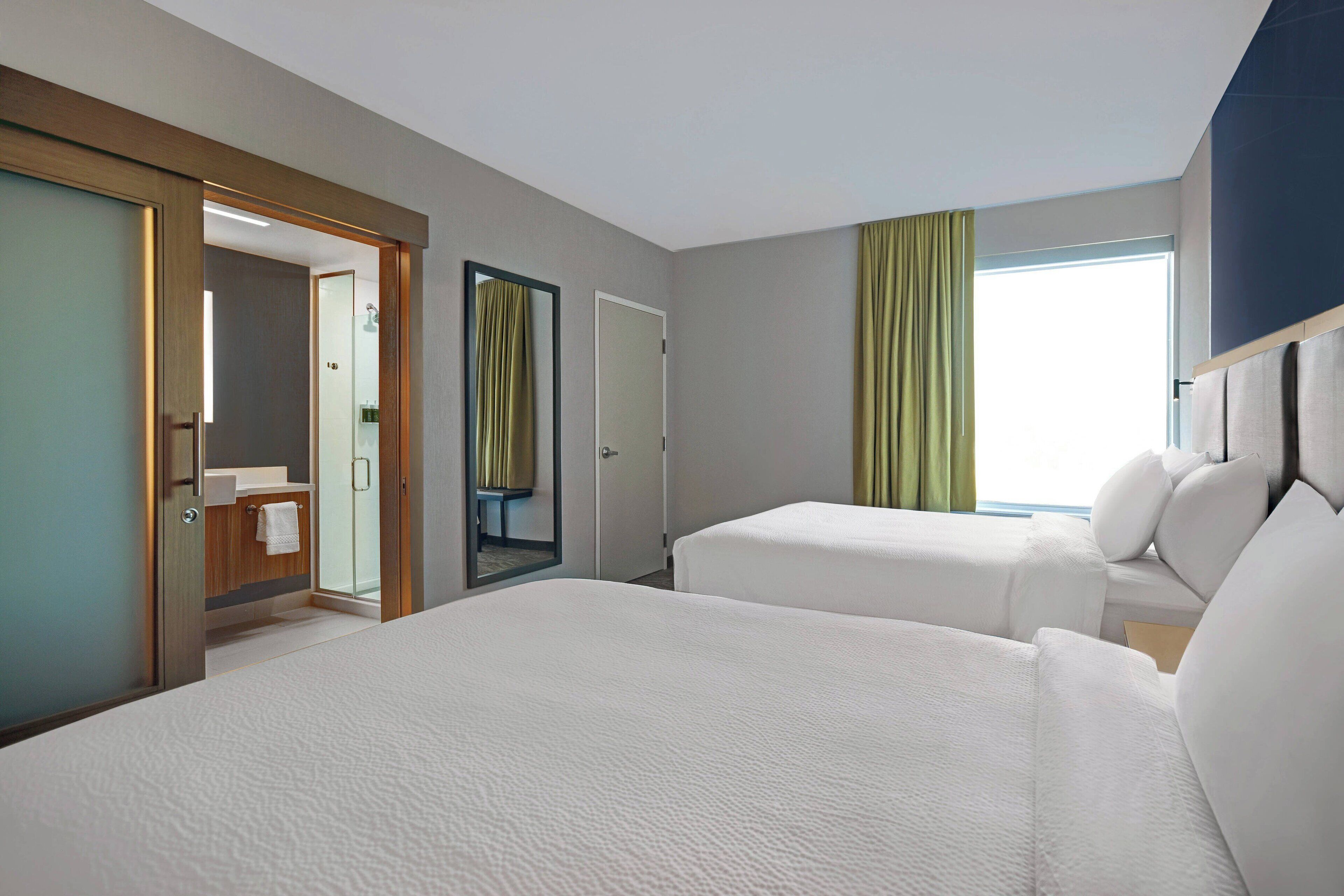 Una habitación de hotel con dos camas, un baño y un ventanal grande con cortinas.