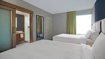 Una habitación de hotel con dos camas, un baño y un ventanal grande con cortinas.