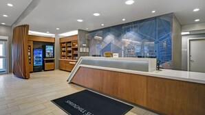A modern hotel reception area with a wooden reception desk, a digital kiosk, and a vending machine. - SpringHill Suites by Marriott St. Paul Arden Hills (Arden Hills)