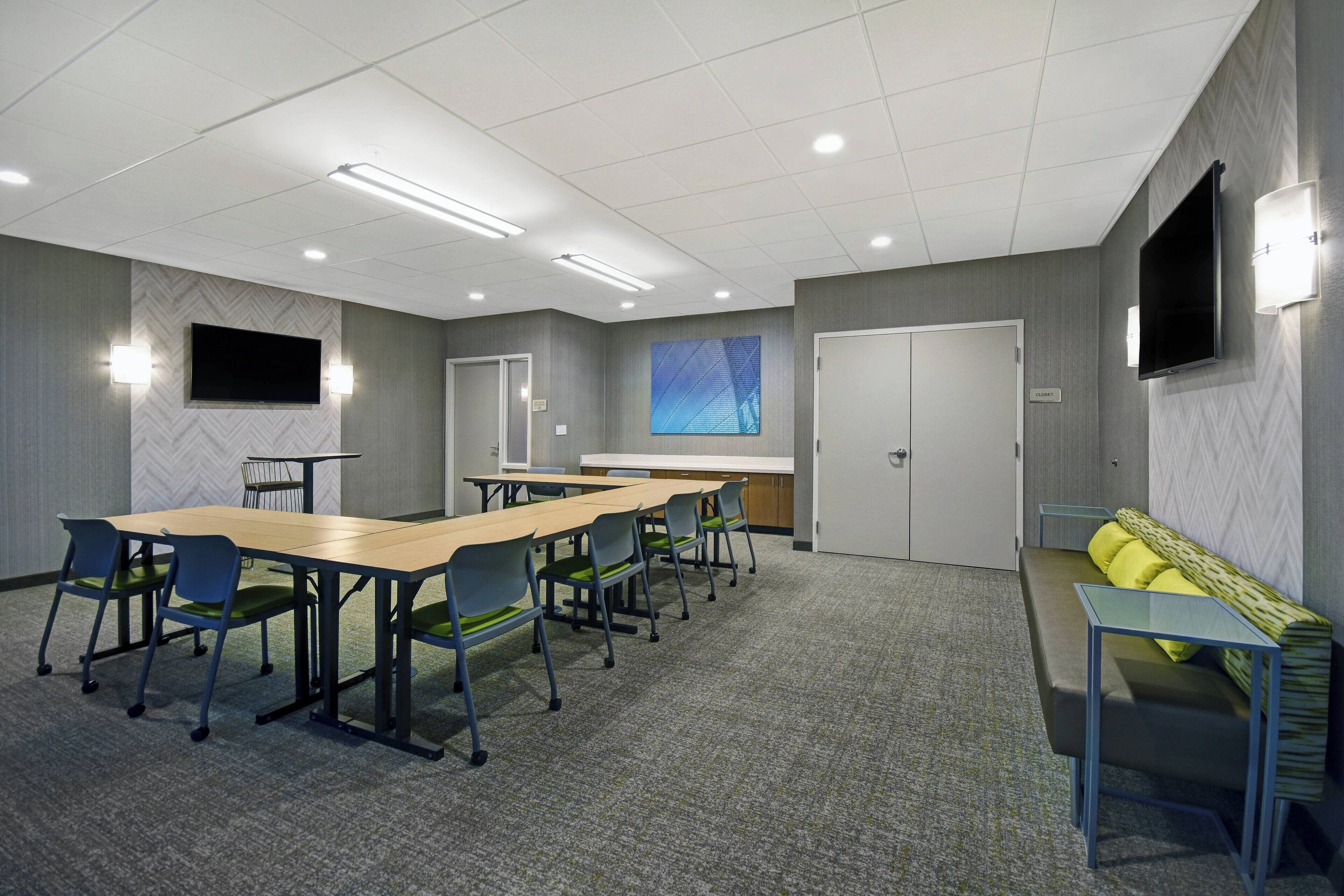 A conference room with a long table, chairs, a sofa, and a TV on the wall.