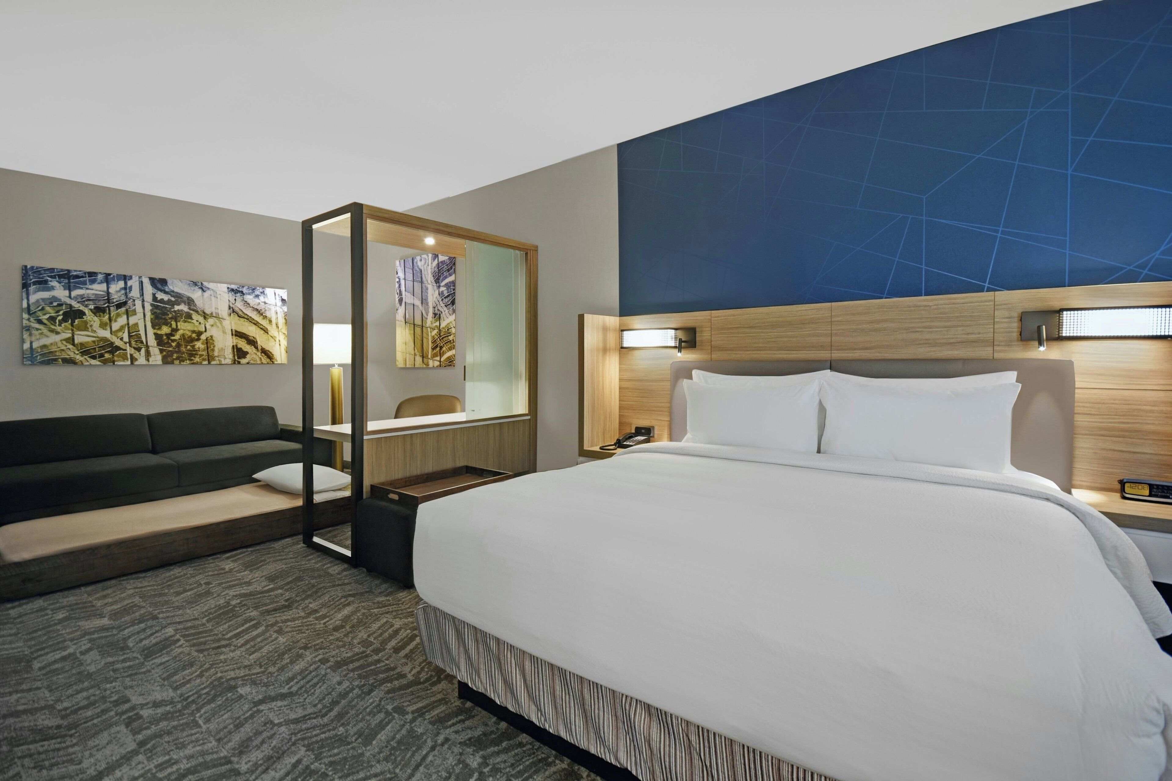 Una habitación de hotel con una cama grande, un sofá, un escritorio y un espejo.