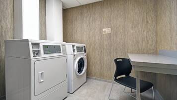 A laundry area with two washing machines, a drying machine, and a table with a chair.