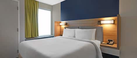 A hotel room with a large bed, a nightstand with a phone, and a window with curtains.