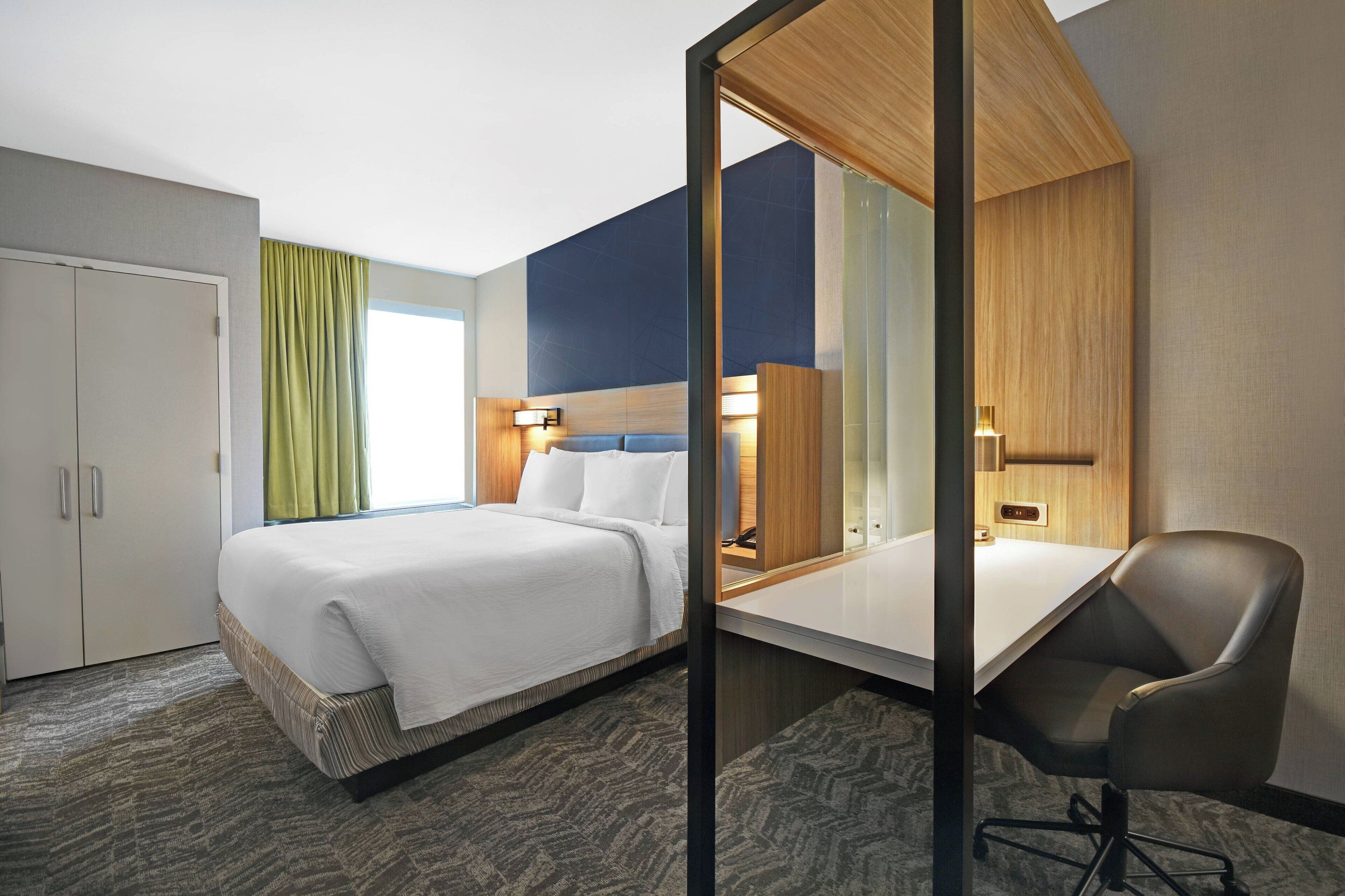 Ein Hotelzimmer mit Bett, Schreibtisch, Stuhl, Kleiderschrank und Blick ins Freie.