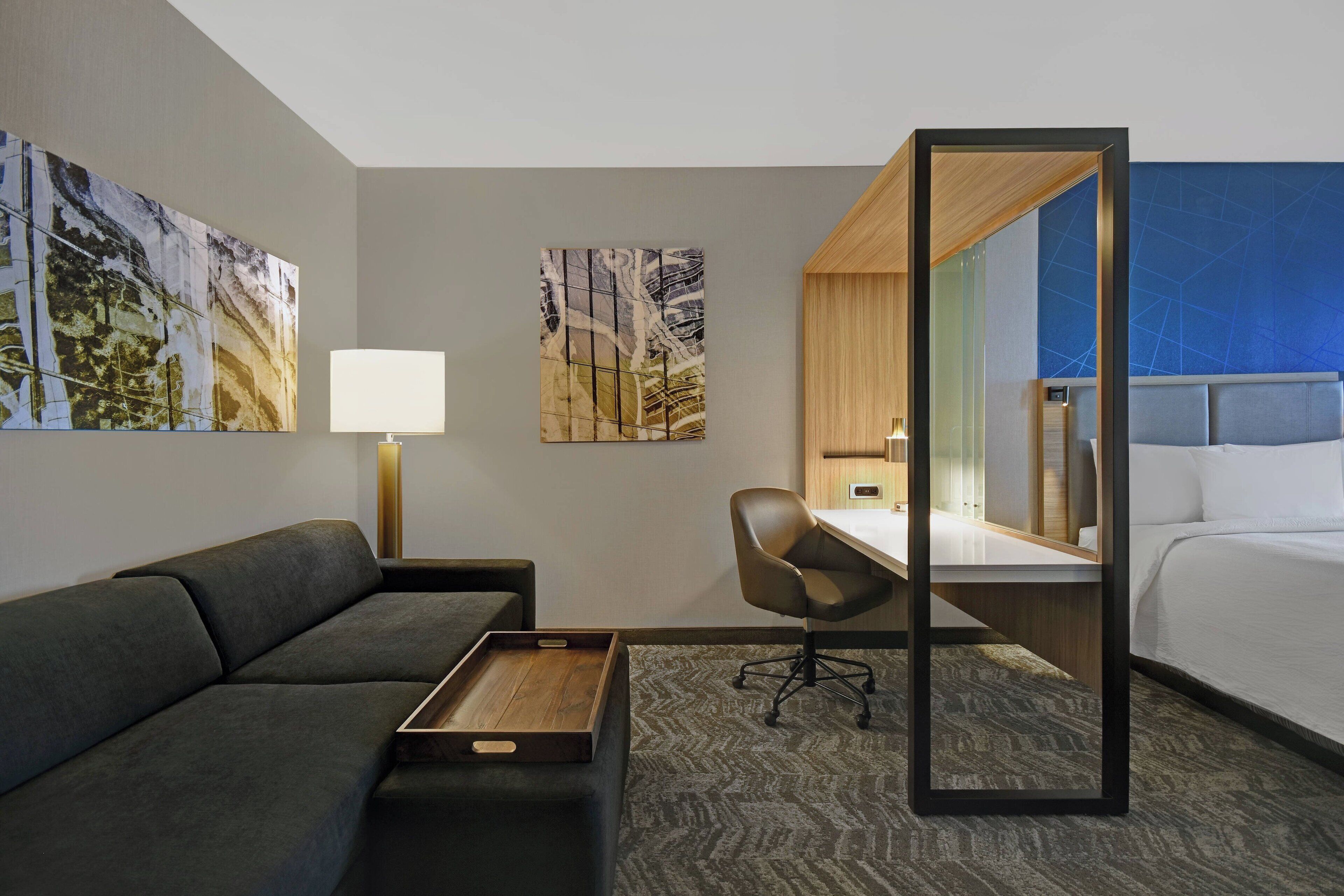A modern hotel room with a sofa, a desk, a chair, a bed, and artwork on the walls.