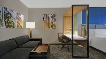 Una habitación de hotel moderna con sofá, escritorio, silla, cama y obras de arte en las paredes.