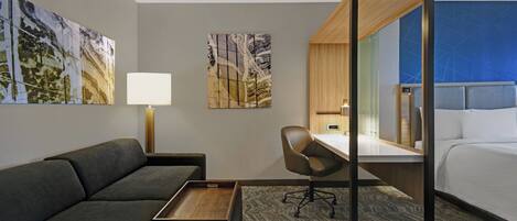 A modern hotel room with a sofa, a desk, a chair, a bed, and artwork on the walls.