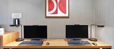 A dual-monitor workstation with two keyboards, two mice, and a framed abstract painting above.