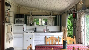 A compact kitchen with white cabinets, a stove, and a microwave. There's a dining area with a wooden table and chairs, and a window with curtains. - 5-Star Park Texel (De Cocksdorp)