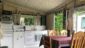 A compact kitchen with white appliances, a dining area with a table and chairs, and a view of greenery outside. - 5-Star Park Texel (De Cocksdorp)