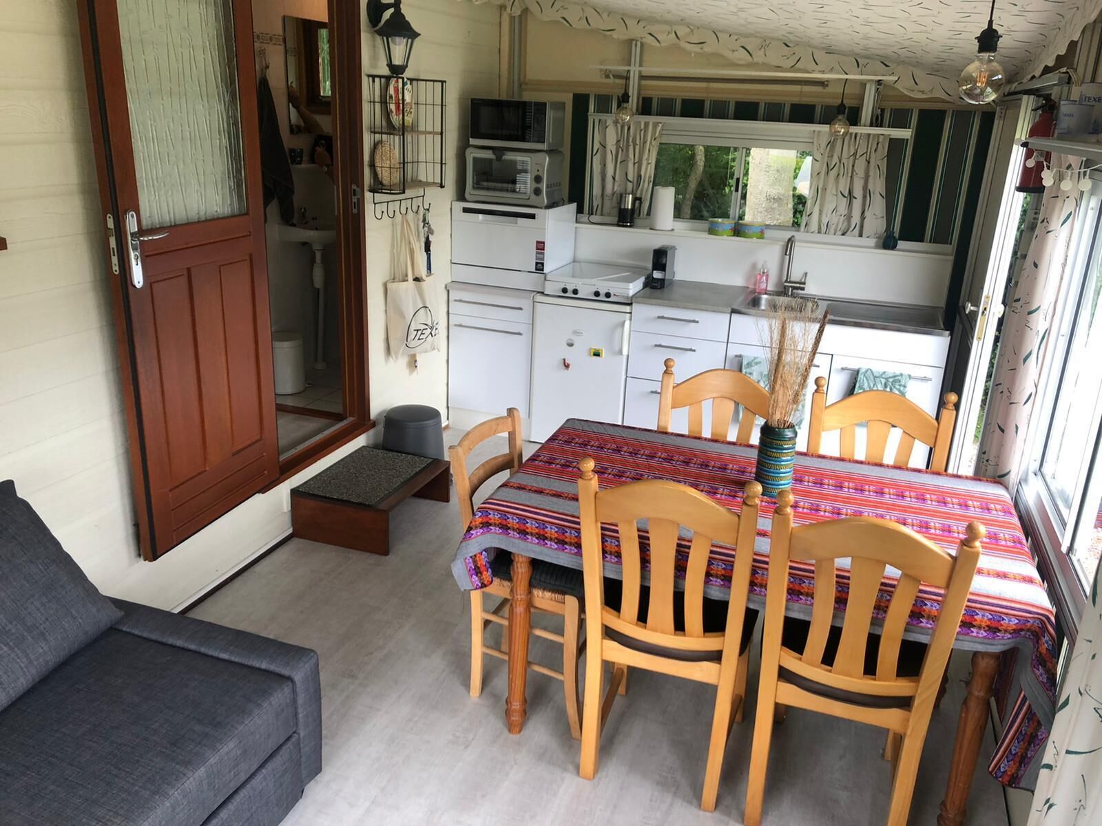Een kleine keuken met een magnetron, fornuis en wastafel. Er is een eettafel met stoelen en een kleine bank in de woonkamer.