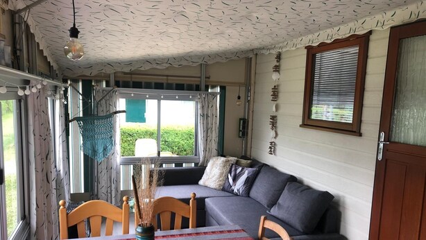 A cozy room with a sofa, a dining table with chairs, a hanging light fixture, and a window with curtains. - 5-Star Park Texel (De Cocksdorp)