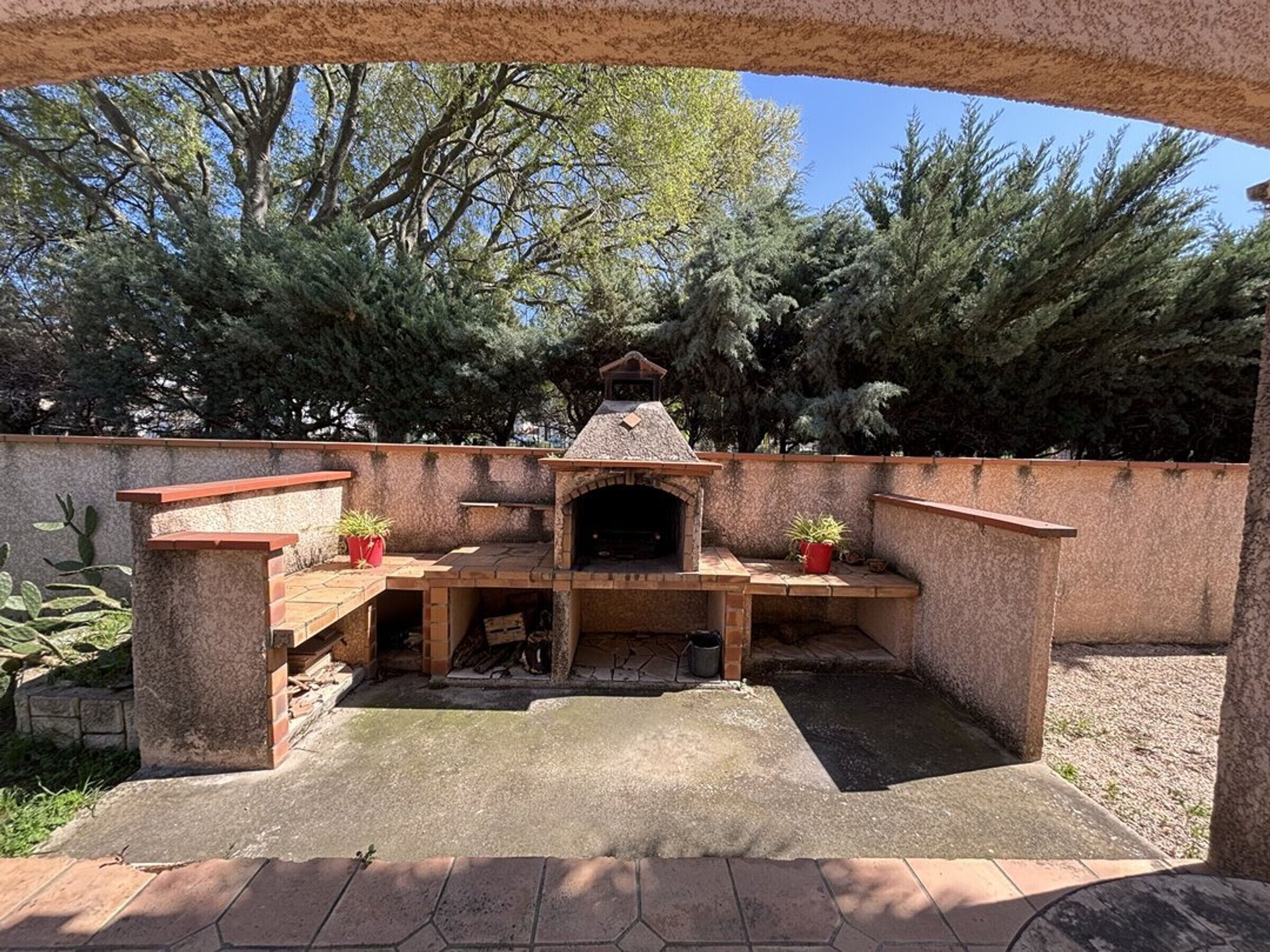 Un espace extérieur aménagé en terrasse, avec un barbecue en pierre et des sièges.
