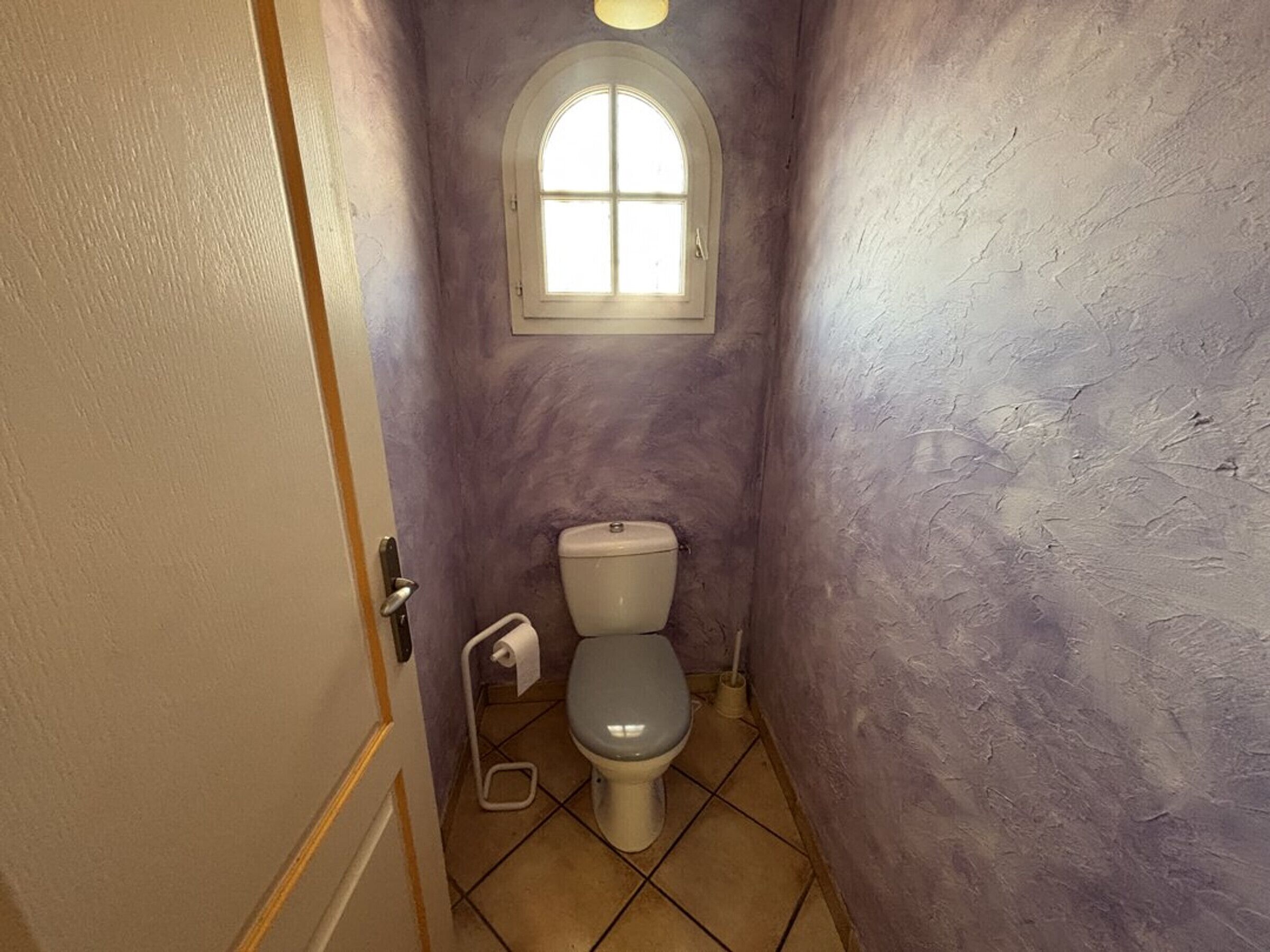 Ein schmales Badezimmer mit Toilette, kleinem Fenster und Tür.