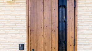 A wooden door with a vertical black security grille, set in a brick wall. - Bon Moment B (Fujikawaguchiko)
