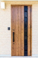 Uma porta de madeira com uma grade de segurança vertical preta, embutida numa parede de tijolos.