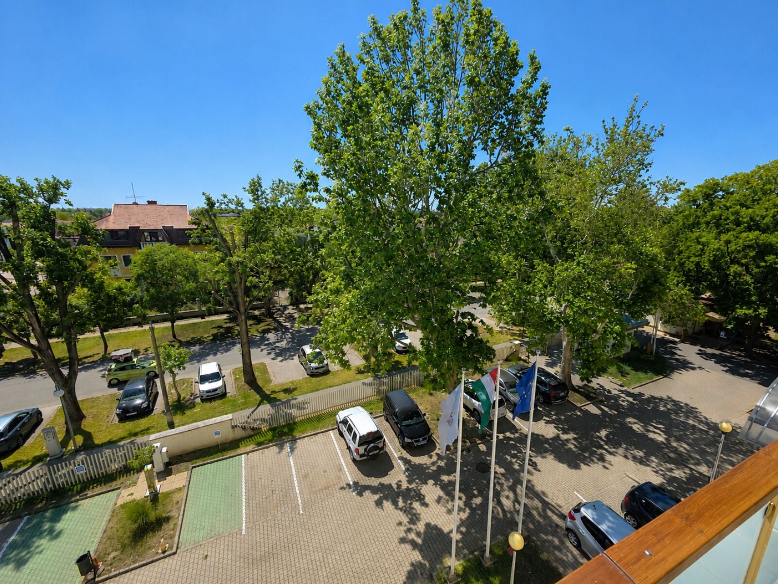 A parking lot with multiple cars, a flagpole with flags, and a building in the background.