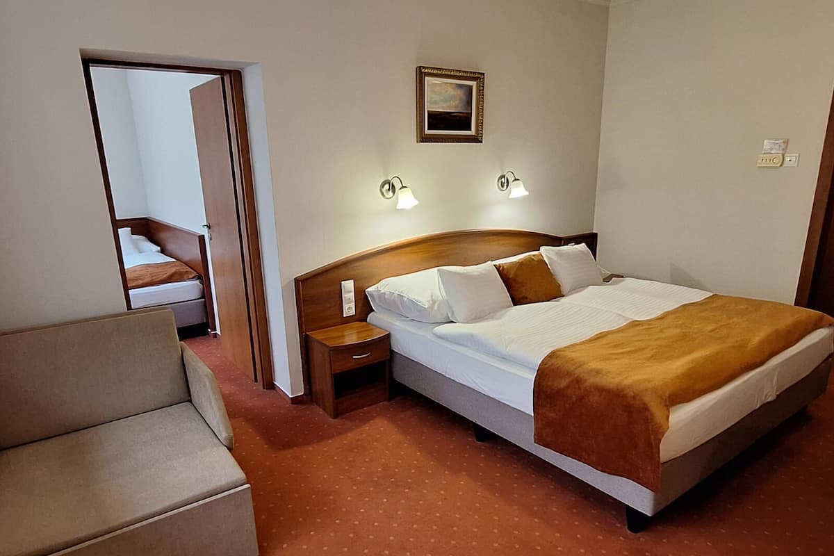 Una habitación de hotel con una cama, una mesita de noche, una lámpara, un cuadro en la pared y una puerta que da a otra habitación.