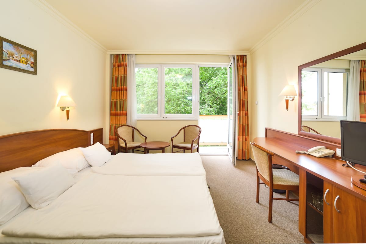 Una habitación de hotel con una cama grande, un escritorio con una computadora, una silla y una ventana con cortinas.