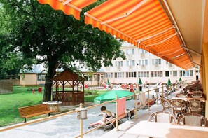 An outdoor seating area with tables and chairs, a gazebo, and a large tree. - Hungarospa Thermal Hotel (Hajduszoboszlo)