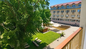 A hotel courtyard with a swimming pool, lounge chairs, and a building with multiple balconies. - Hungarospa Thermal Hotel (Hajduszoboszlo)
