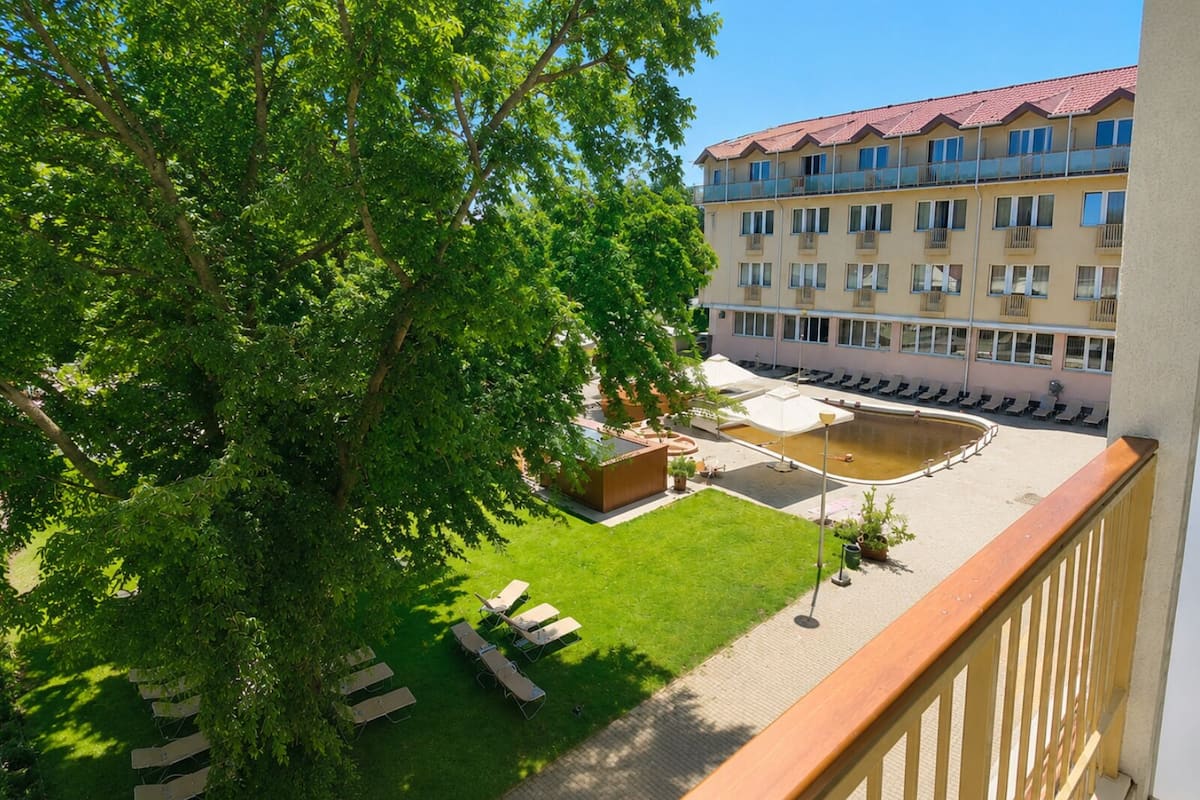 Un patio de hotel con piscina, sillones de descanso y un edificio con varios balcones.