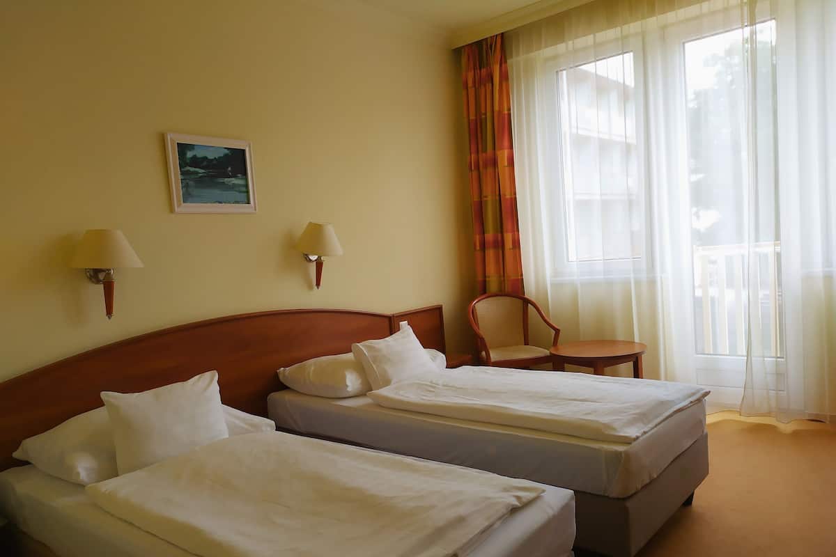 Habitación de hotel con dos camas, una silla, una mesa y una ventana con cortinas.