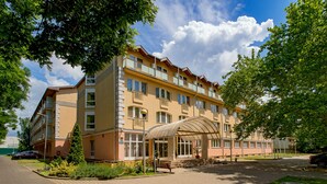 A multi-story hotel with a covered entrance, a parking area, and a well-maintained garden. - Hungarospa Thermal Hotel (Hajduszoboszlo)