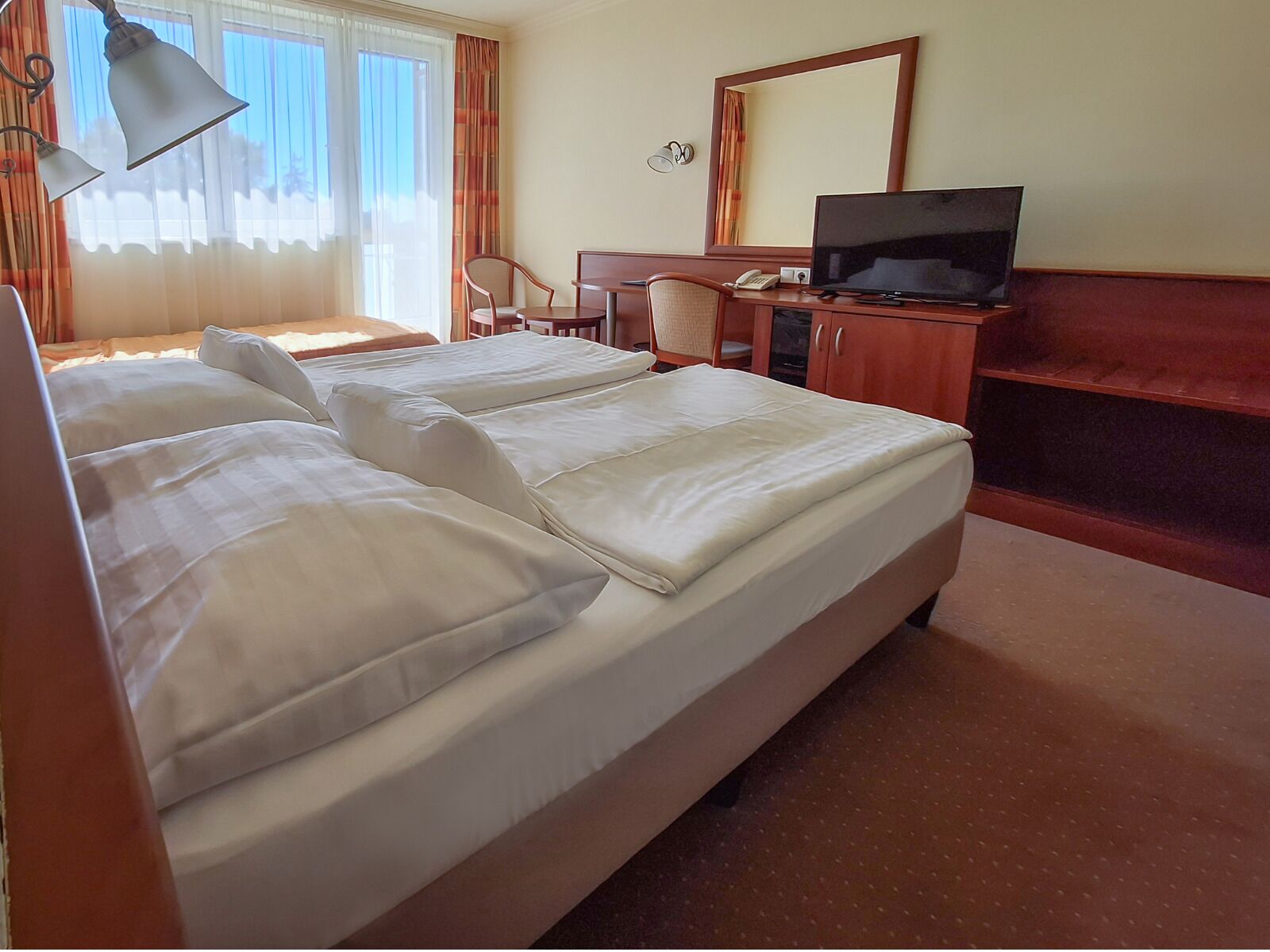 A hotel room with a large bed, a desk with a TV, and a chair.