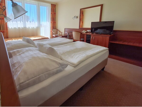 Una habitación de hotel con una cama grande, un escritorio con televisor y una silla.