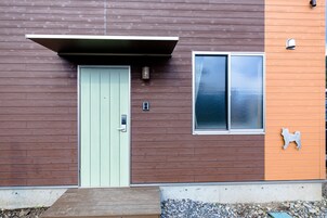 A modern building with a green door, a window with frosted glass, and a small dog cutout on the orange wall.