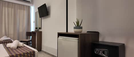 A hotel room with a bed, a desk, a television, a small refrigerator, and a wood-burning stove.