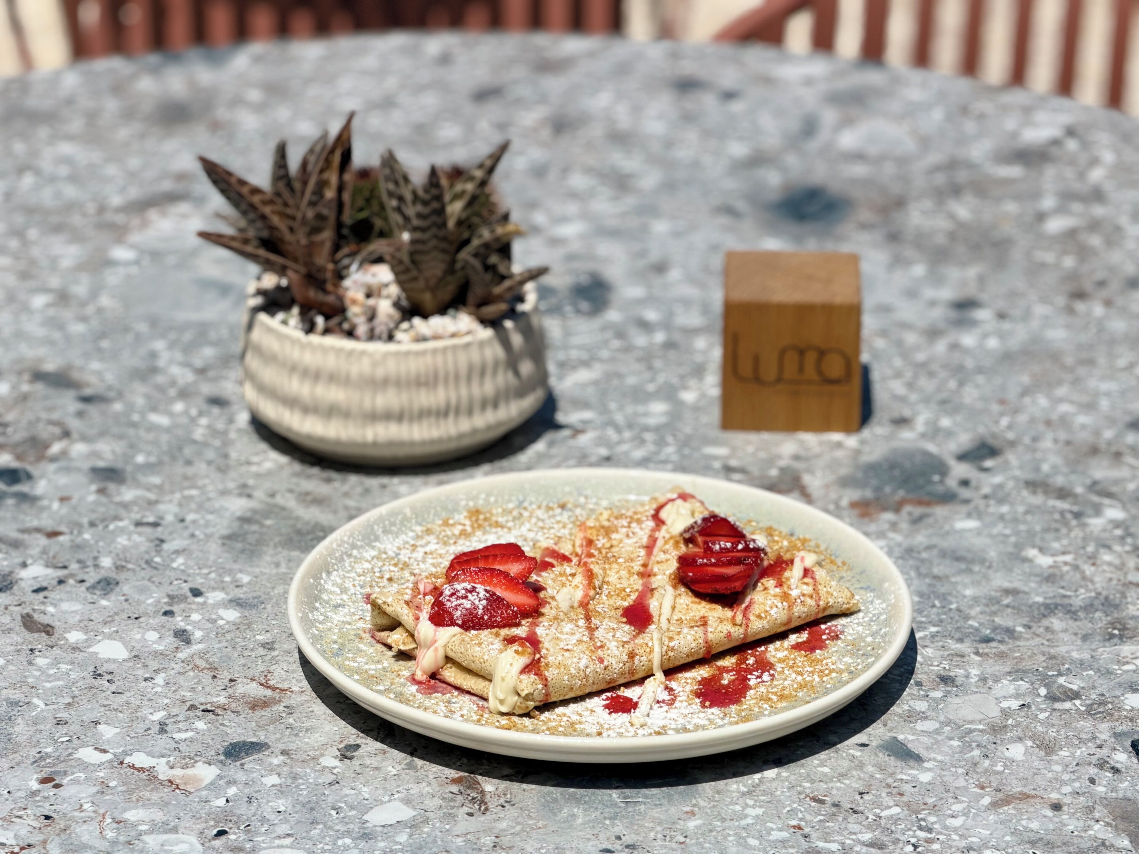 Un plato de crepas con fresas y azúcar glas sobre una mesa.