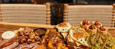 A wooden table with a variety of food items including pastries, potatoes, and a bowl of dipping sauce.