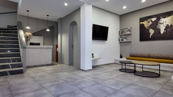 Un moderno vestíbulo de hotel con una recepción, una escalera, una zona de estar con sofá y mesa de centro, un televisor de pantalla plana en la pared y una obra de arte con un mapa mundial.
