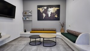 A modern living room with a sofa, two round tables, a world map artwork, and a TV. - Hotel Santorini (Santorini)