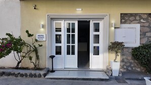 A hotel entrance with a double door, a sign reading "HOTEL SANTORINI", and a small garden area with plants. - Hotel Santorini (Santorini)