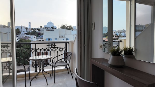 A balcony with a table and chairs, a potted plant, and a view of white buildings and a church. - Hotel Santorini (Santorini)