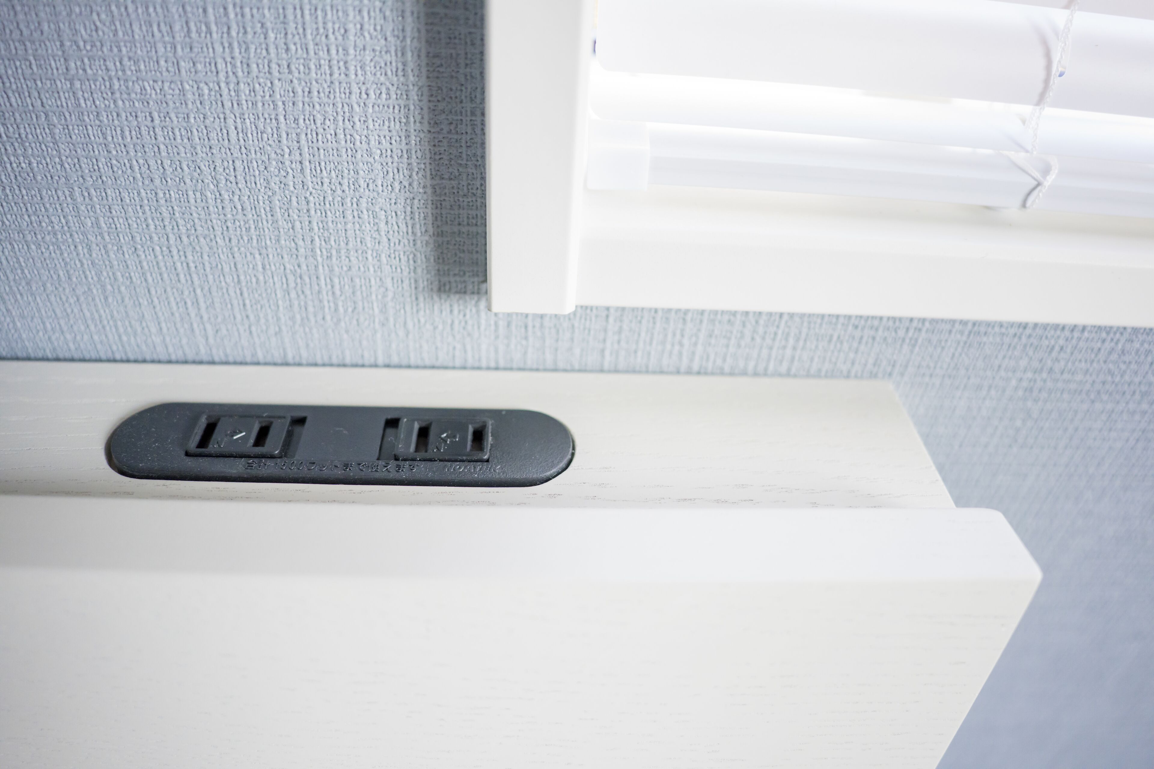 A white bedside table with a power outlet and a small control panel.