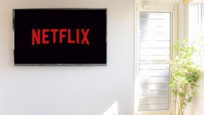 Televisão de tela plana montada em parede branca, com a palavra "NETFLIX" em letras vermelhas.