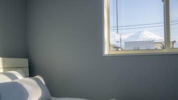 A bedroom with a bed, pillows, a nightstand, and a window overlooking a snowy mountain.